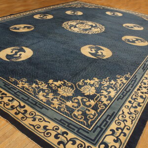 Large indigo rug with tan medallions and geometric fretwork pattern lies on hardwood flooring.