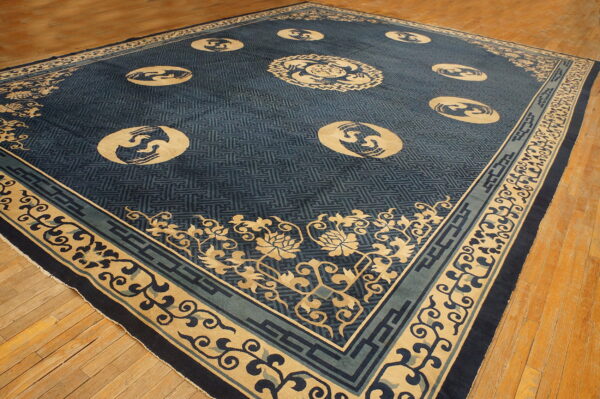 Large indigo rug with tan medallions and geometric fretwork pattern lies on hardwood flooring.