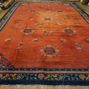Rust orange rug with scattered floral medallions and a wide navy blue patterned border on a wood floor.