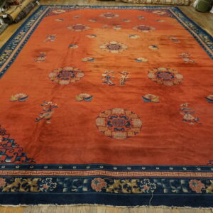 Rust orange rug with dark blue floral borders and medallions lying on a wooden floor.