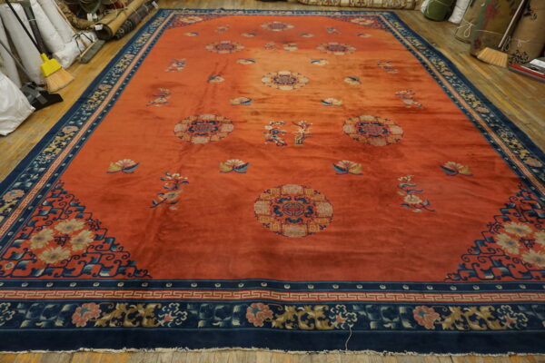 Rust orange rug with dark blue floral borders and medallions lying on a wooden floor.