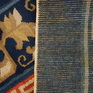 Close-up showing the plush navy and tan patterned rug face next to its tightly woven blue and beige backing.
