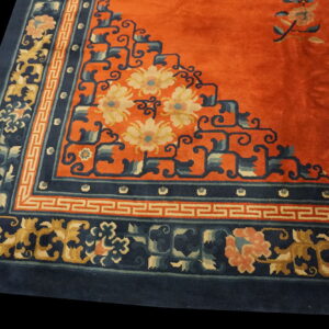 Orange rug field with a stepped corner design and wide navy border featuring floral and meander patterns.