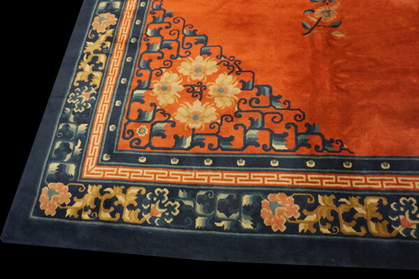 Orange rug field with a stepped corner design and wide navy border featuring floral and meander patterns.