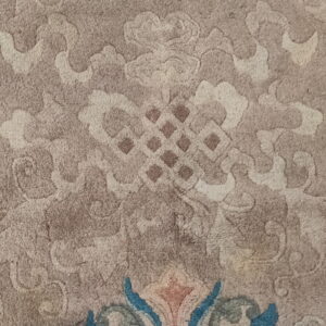 Detail of a carved beige rug featuring subtle scrolling patterns and a prominent colorful blue and pink floral edge.