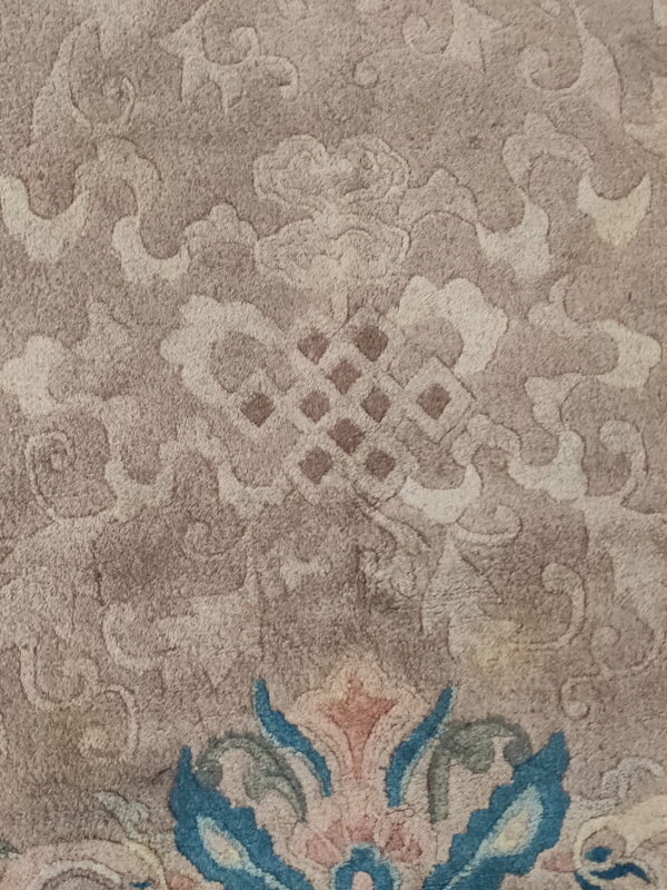 Detail of a carved beige rug featuring subtle scrolling patterns and a prominent colorful blue and pink floral edge.