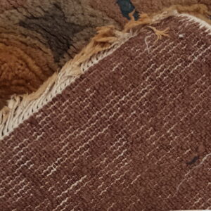 Close-up showing the shaggy brown pile folded back to reveal the tight, striped woven rug backing.