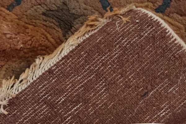 Close-up showing the shaggy brown pile folded back to reveal the tight, striped woven rug backing.