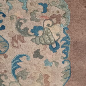 Textured rug detail showing ornate blue, teal, and brown motifs on beige, bordering a solid mauve area.