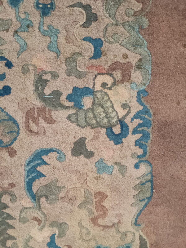 Textured rug detail showing ornate blue, teal, and brown motifs on beige, bordering a solid mauve area.