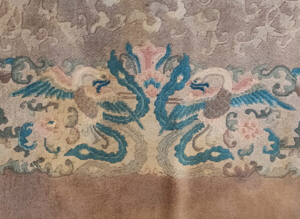 Muted low-pile rug detail features teal blue, pink, and tan stylized mirrored animal and floral motifs.