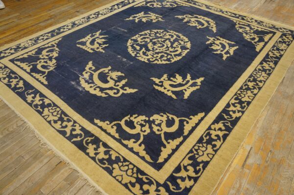 Navy and gold low-pile rug featuring a medallion pattern, displayed on worn wooden plank flooring.