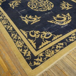 Navy blue rug with gold ornate scrollwork borders lies on worn, light brown wood planks.