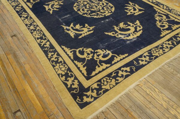 Navy blue rug with gold ornate scrollwork borders lies on worn, light brown wood planks.