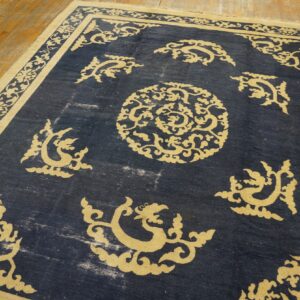 Dark blue rug with a contrasting gold traditional scrolling pattern rests on light wood planks.