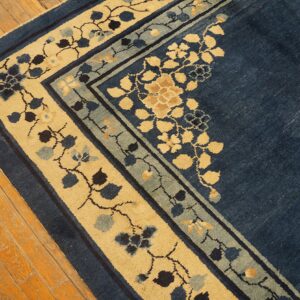 Corner of a navy blue rug with thick tan and light blue floral borders on distressed wood flooring.