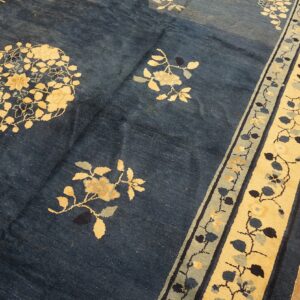 Dark blue rug with cream and slate floral patterns and a wide botanical border rests on wood plank flooring.