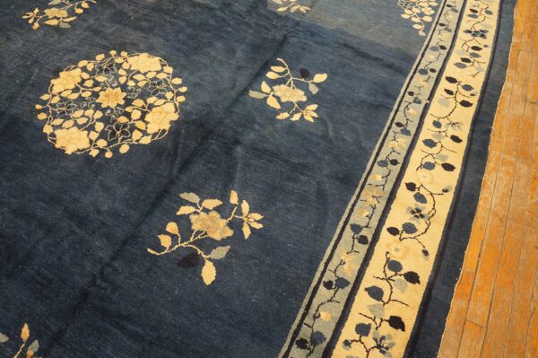 Dark blue rug with cream and slate floral patterns and a wide botanical border rests on wood plank flooring.