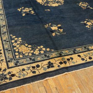 Navy blue rug featuring scattered floral designs and wide beige patterned borders on wood plank flooring.