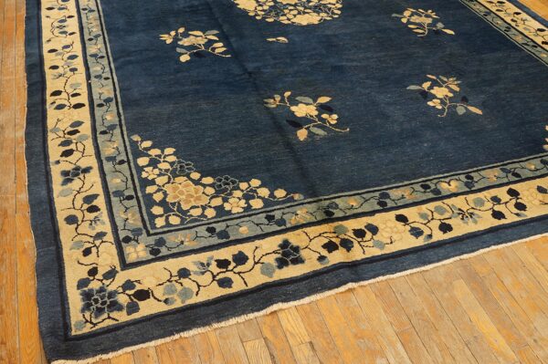 Navy blue rug featuring scattered floral designs and wide beige patterned borders on wood plank flooring.