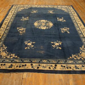 Dark blue rug features scattered light floral motifs and a detailed cream and light blue border on wood flooring.