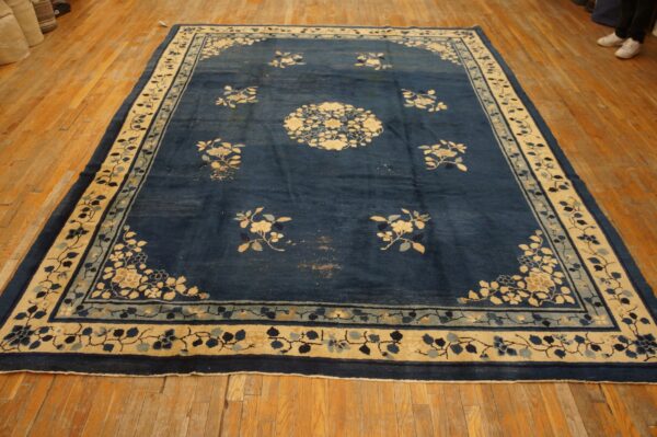 Dark blue rug features scattered light floral motifs and a detailed cream and light blue border on wood flooring.