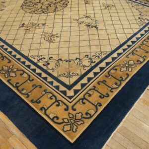 Corner detail of a beige lattice rug featuring a gold and navy floral border on light plank wood flooring.