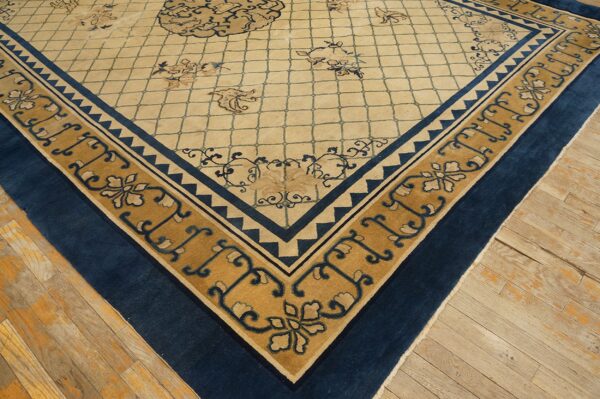 Corner detail of a beige lattice rug featuring a gold and navy floral border on light plank wood flooring.