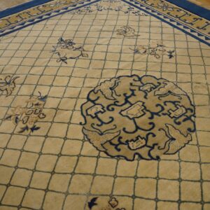 Tan lattice rug featuring blue and tan botanical motifs and thick navy blue borders on wood flooring.