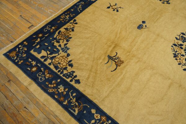 Golden yellow rug with a dark blue floral pattern border rests on rustic exposed wood flooring.