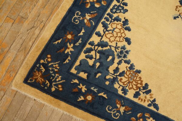 Yellow rug corner with a navy blue and rust floral border resting on distressed wood floors.
