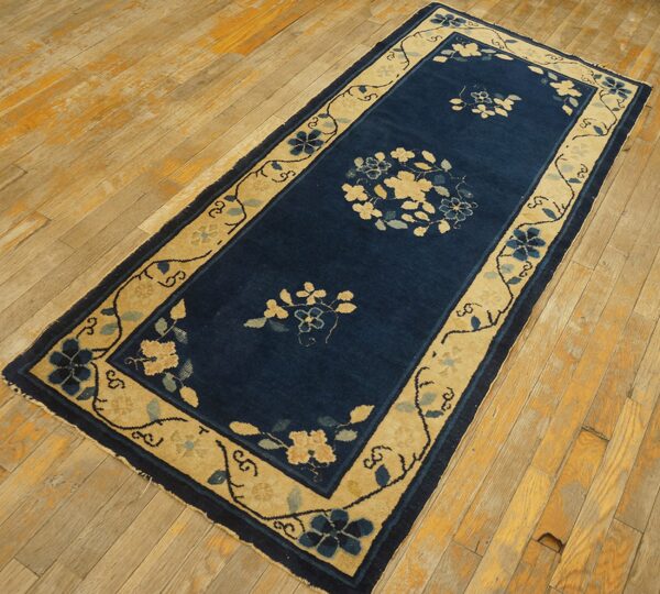 Blue floral runner rug with a wide tan border sits on exposed, light-colored wooden floorboards.