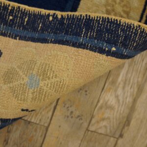 Close-up of a tan rug with navy blue border curled on distressed light wood planks.