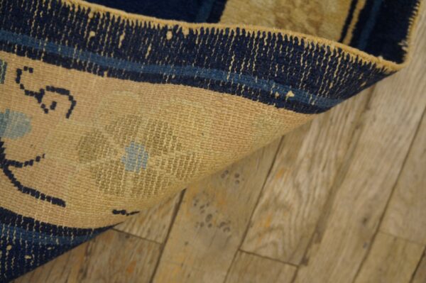 Close-up of a tan rug with navy blue border curled on distressed light wood planks.