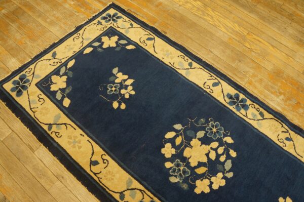 Navy blue runner rug with golden cream floral border sits on light, rustic wood floors.