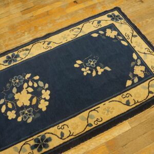 Dark blue rug with a wide, pale yellow border and stylized floral vine patterns rests on wood flooring.