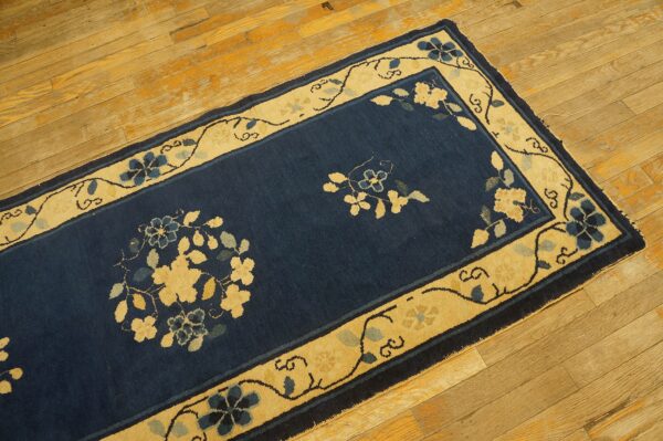 Dark blue rug with a wide, pale yellow border and stylized floral vine patterns rests on wood flooring.