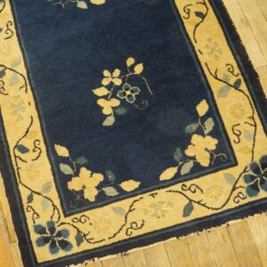 Navy blue rug featuring an ornate yellow and light blue floral border rests on light wood floors.