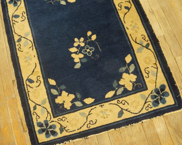 Navy blue rug featuring an ornate yellow and light blue floral border rests on light wood floors.