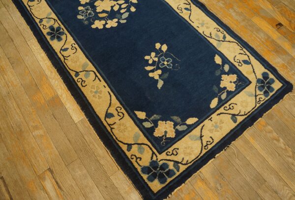 Navy and tan floral runner rug on distressed light brown hardwood floor.