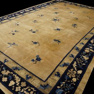 A golden beige rug with sparse blue motifs and complex navy blue floral and geometric borders.