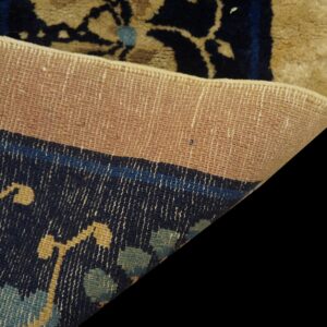 A rug corner is folded, contrasting the tightly woven tan backing with the navy blue patterned pile.