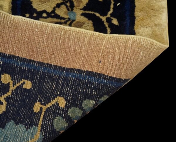 A rug corner is folded, contrasting the tightly woven tan backing with the navy blue patterned pile.