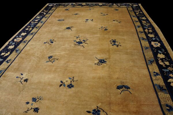 Tan low-pile rug with sparse blue floral sprays and a wide navy border featuring geometric and floral designs.