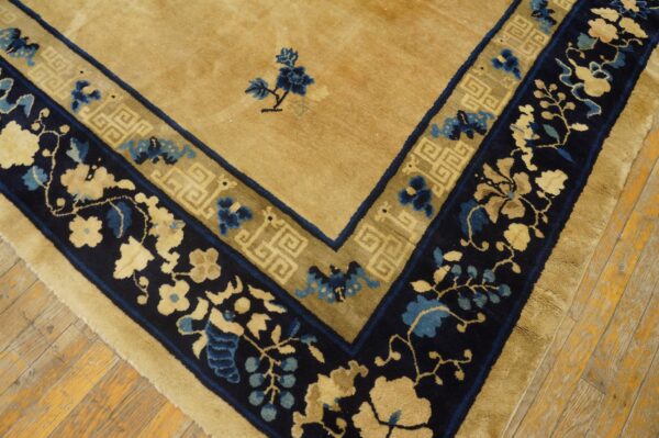 Tan rug with a navy, gold, and blue floral and geometric border on distressed wood floors.