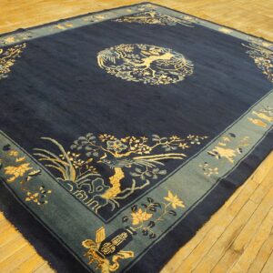 Dark blue rug with gold and light blue traditional motifs and a wide teal border on wood floors.