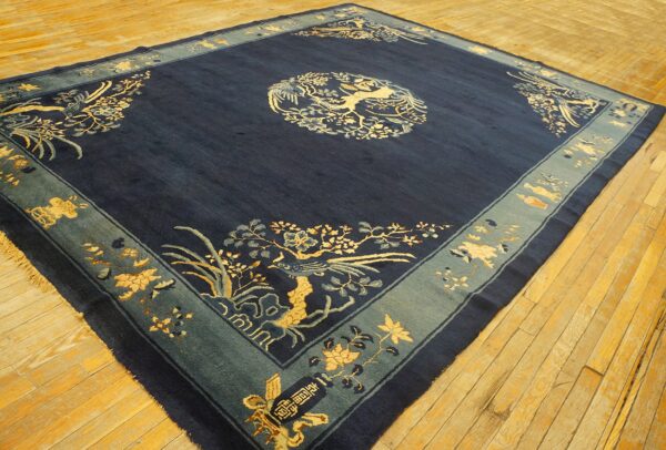 Dark blue rug with gold and light blue traditional motifs and a wide teal border on wood floors.