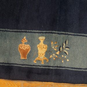 Dark blue rug with a slate border showing ornate tan and rust vases and foliage on a wood floor.