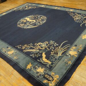 Navy blue rug with a light blue border featuring detailed cream bird and floral patterns on wood floors.