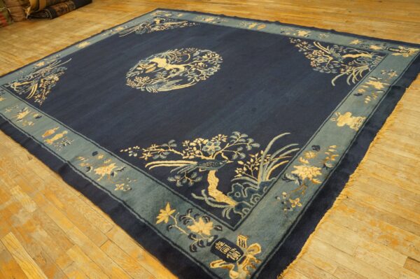 Navy blue rug with a light blue border featuring detailed cream bird and floral patterns on wood floors.